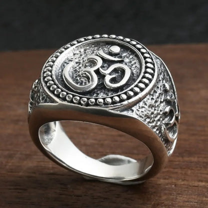 Bague argent bouddhiste homme posée sur surface en bois, motif Om visible